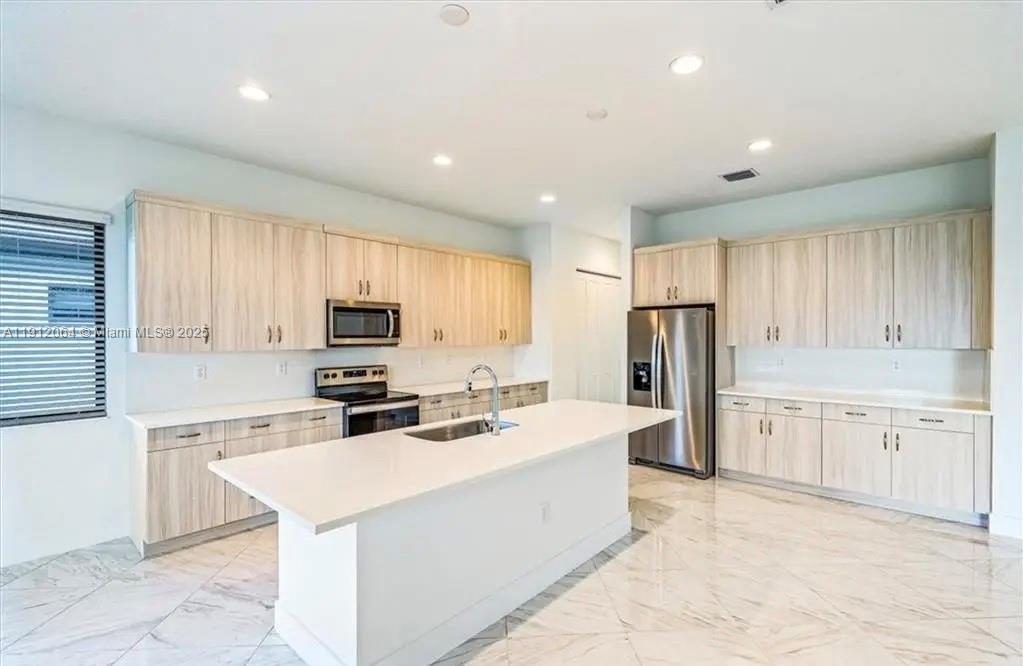 A modern kitchen features light wood cabinets, white countertops, a central island, and marble flooring — 5048 GAMBERO WAY, Ave Maria FL 34142, AVE MARIA, FL