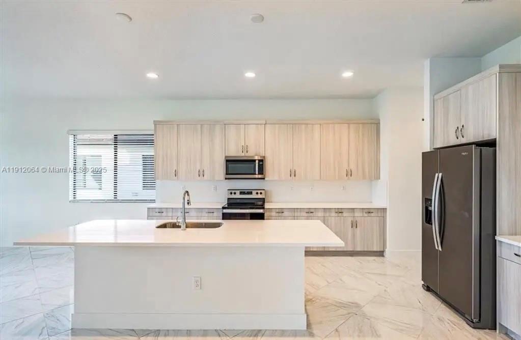 A modern kitchen features light wood cabinets, white countertops, a central island, and stainless appliances — 5048 GAMBERO WAY, Ave Maria FL 34142, AVE MARIA, FL
