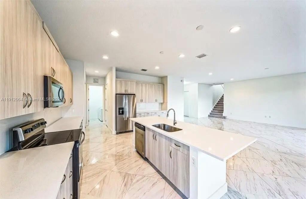 A modern kitchen features light wood cabinets, a white island, and marble-patterned tile flooring — 5048 GAMBERO WAY, Ave Maria FL 34142, AVE MARIA, FL