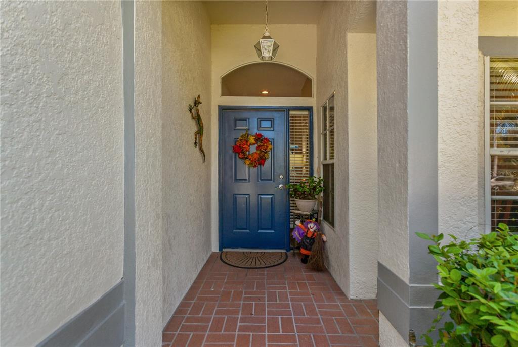 A blue front door with a wreath sits under a covered entryway with brick flooring — 19029 CALLAWAY COURT, TAMPA, FL
