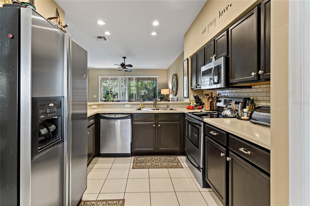A kitchen with dark cabinets, stainless steel appliances, and tile flooring opens to a living area — 19029 CALLAWAY COURT, TAMPA, FL