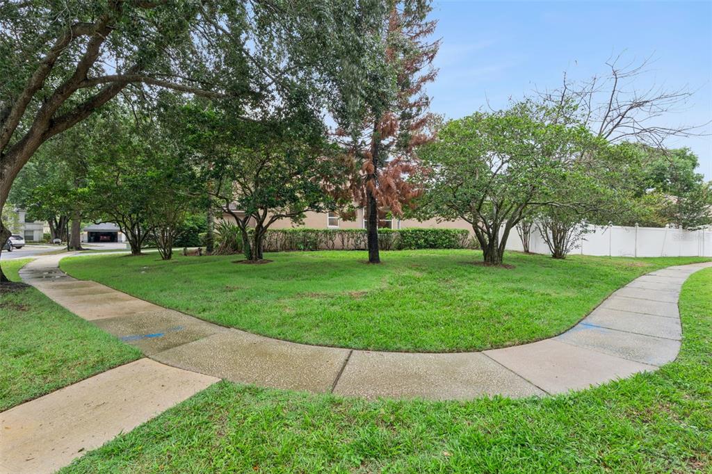 A curved concrete sidewalk borders a grassy lawn with several trees in front of a house — 1025 OCEANBREEZE COURT, ORLANDO, FL