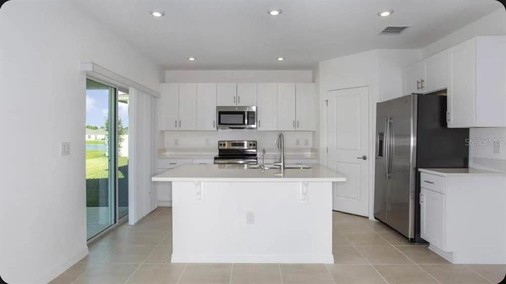 A modern kitchen features white cabinets, stainless steel appliances, a center island, and tile flooring — 13317 COMMONS AVENUE, PARRISH, FL