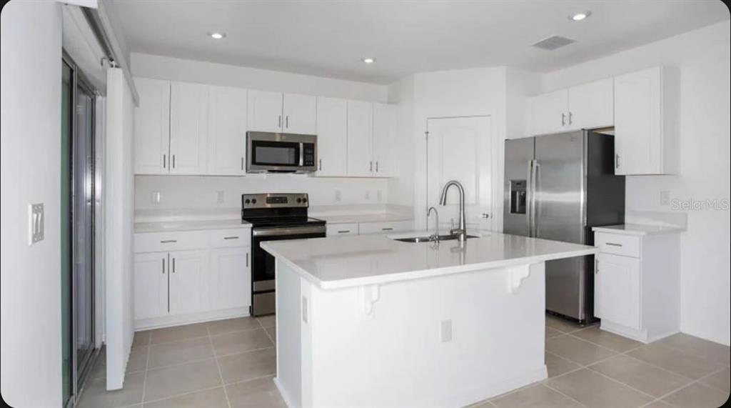 A modern kitchen features white cabinets, stainless steel appliances, and a central island with seating — 13317 COMMONS AVENUE, PARRISH, FL