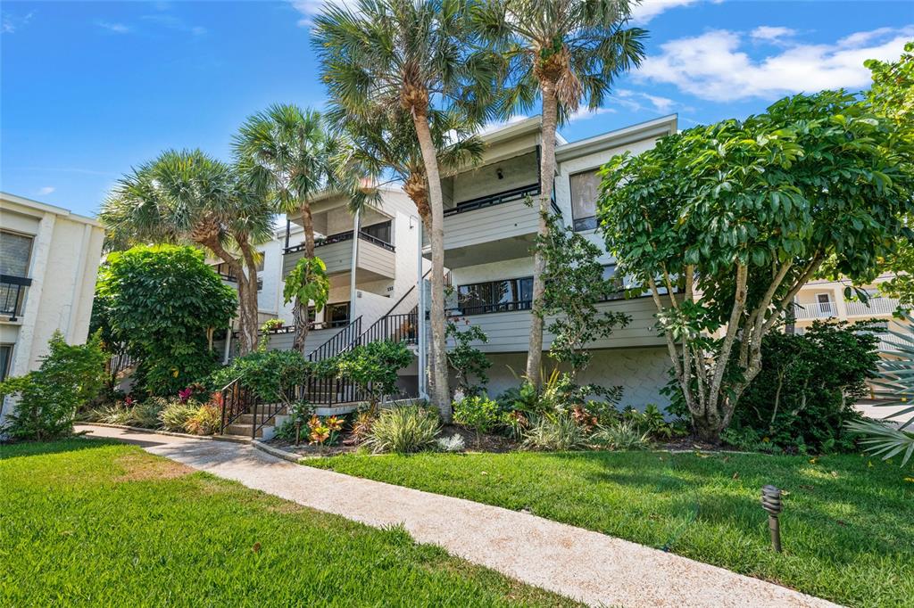 A multi-story residential building with balconies, stairs, and palm trees in a landscaped yard — 1555 TARPON CENTER DRIVE UNIT 156, VENICE, FL