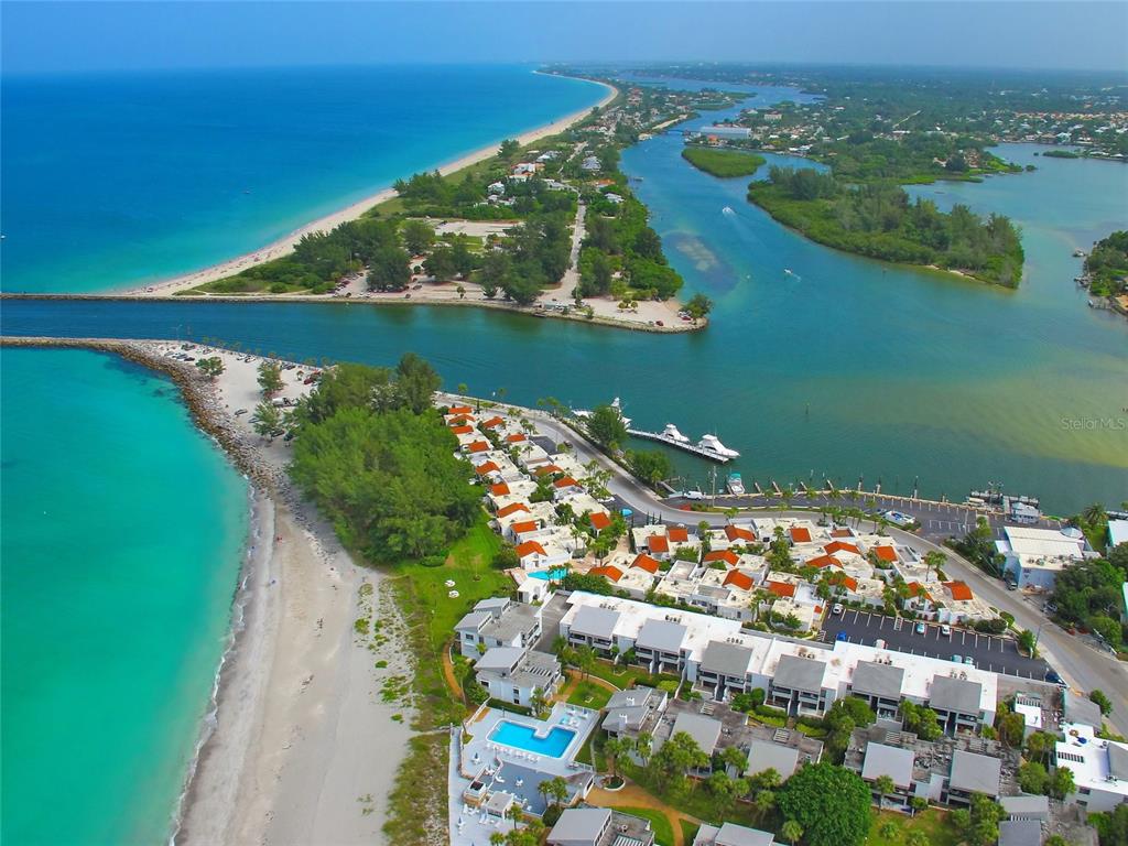 An aerial view shows a coastal resort with a beach, inlet, and residential buildings — 1555 TARPON CENTER DRIVE UNIT 156, VENICE, FL