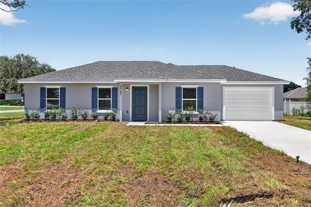 A single-story house with gray siding, blue shutters, a dark front door, and a garage — 6747 SW 86TH PLACE, OCALA, FL