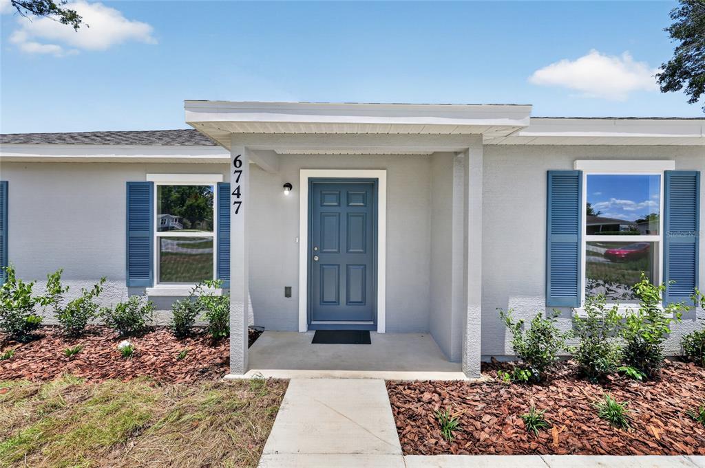 A gray house exterior features a blue front door, blue shutters, and a concrete walkway — 6747 SW 86TH PLACE, OCALA, FL