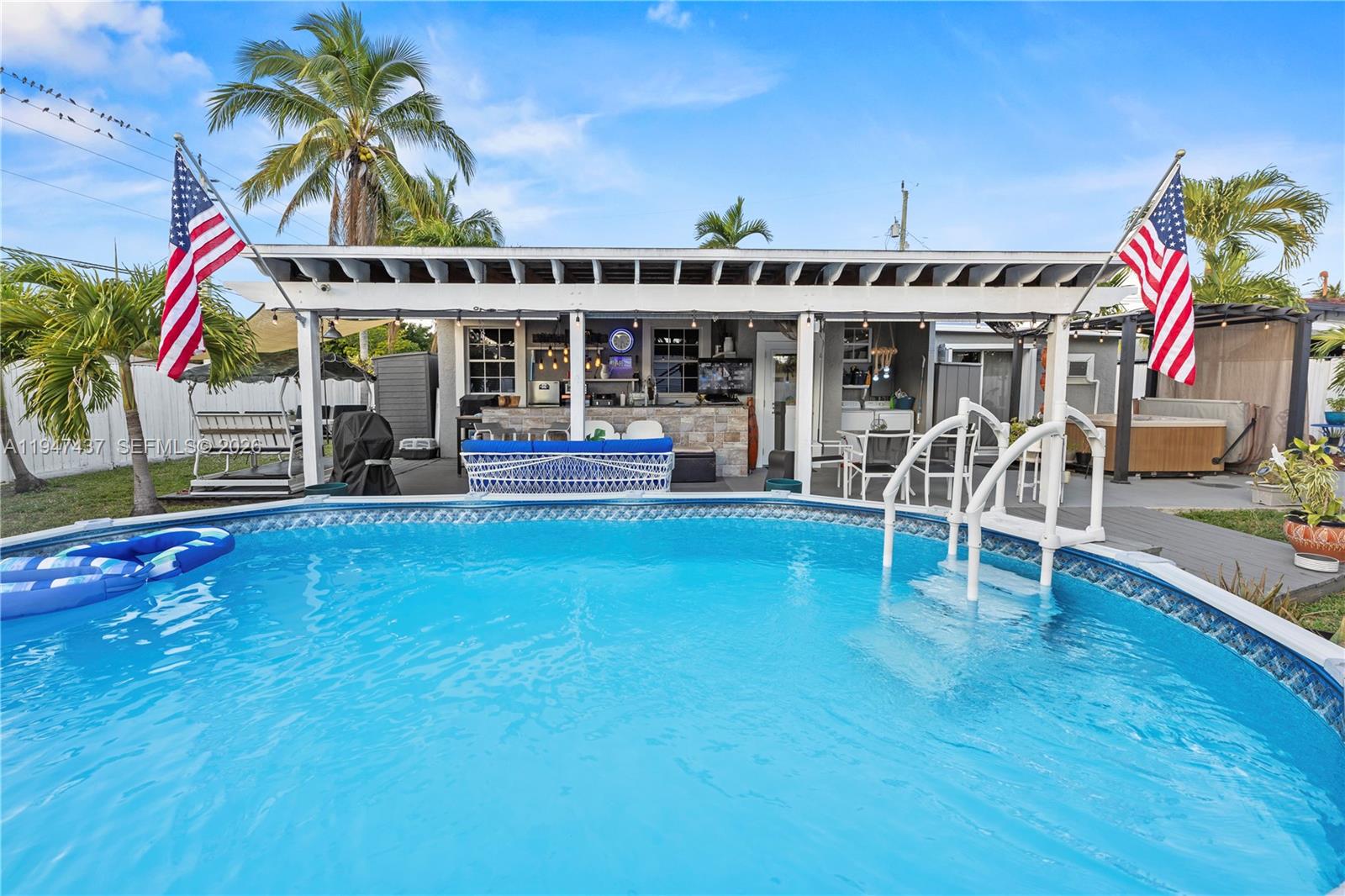 An outdoor patio with a bar and pool area features two American flags — 117 SW 6th St, Hallandale Beach FL 33009, HALLANDALE BEACH, FL