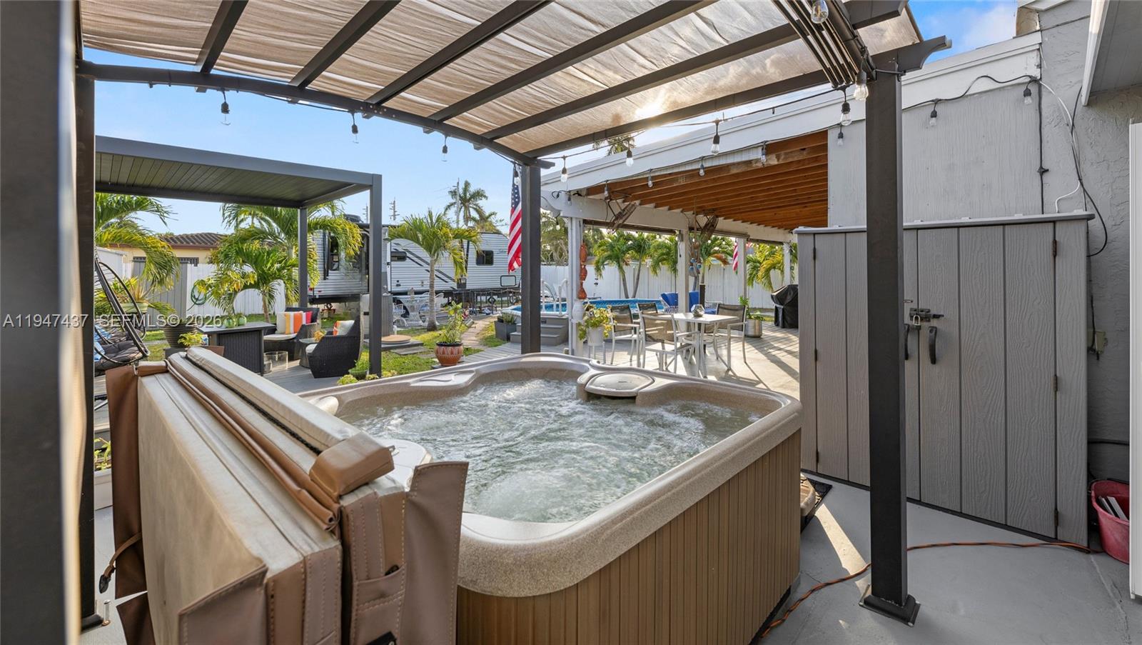A hot tub sits on a patio under a pergola next to a storage shed — 117 SW 6th St, Hallandale Beach FL 33009, HALLANDALE BEACH, FL