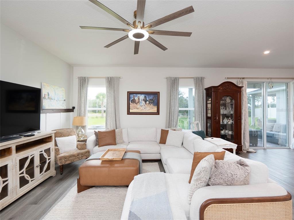A living room features a white sectional sofa, a leather ottoman, and a ceiling fan — 11026 HIGH NOON TRAIL, PARRISH, FL