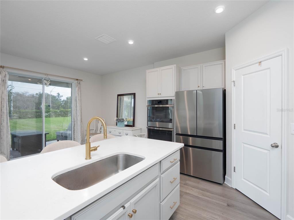 A kitchen features a white island with a sink, stainless steel appliances, and light cabinetry — 11026 HIGH NOON TRAIL, PARRISH, FL