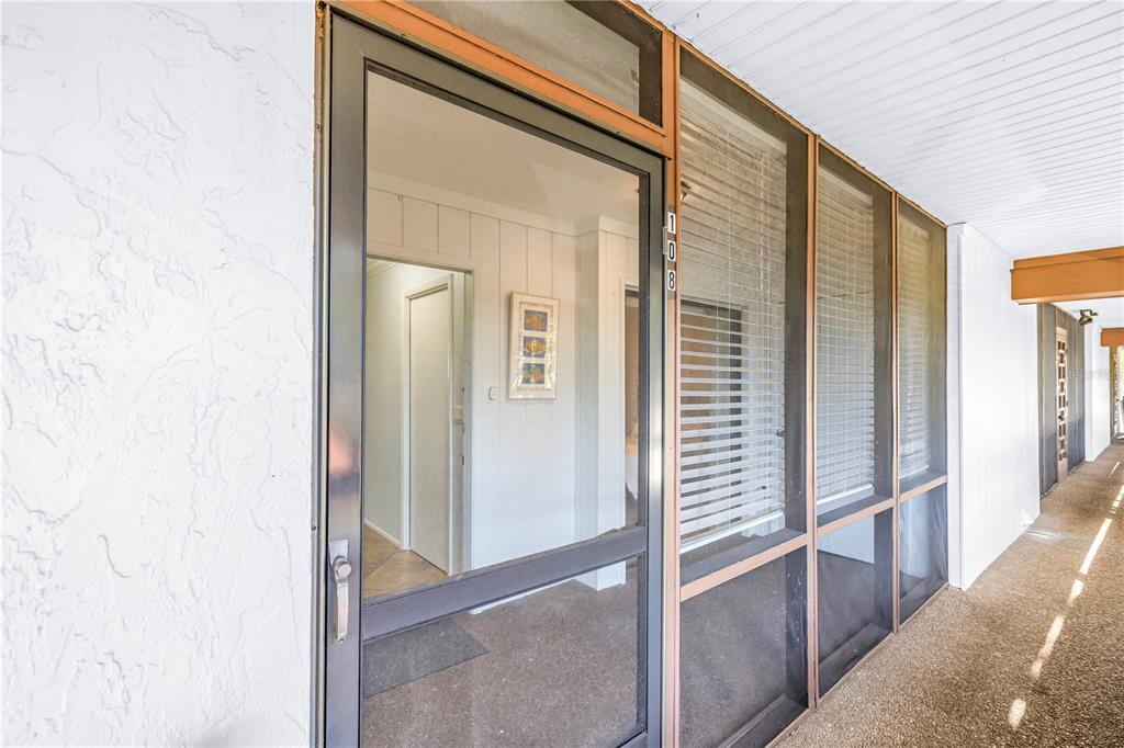 A ground-level apartment entrance features a screen door, large windows with blinds, and a walkway — 3500 EL CONQUISTADOR PARKWAY UNIT 108, BRADENTON, FL