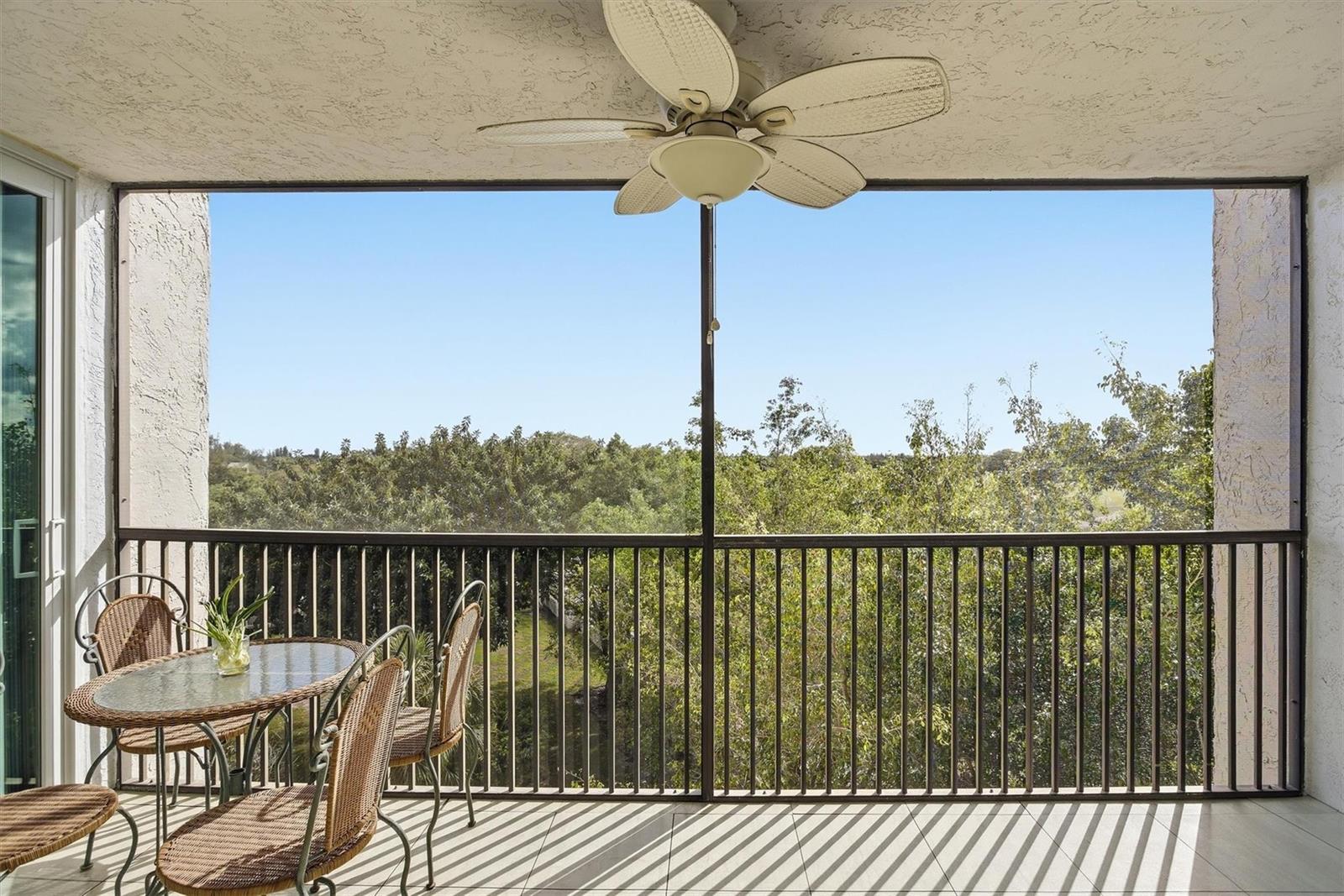 A screened-in balcony features a ceiling fan, wicker patio furniture, and a view of trees — 3910 Inverrary Boulevard # B, Lauderhill FL 33319, LAUDERHILL, FL