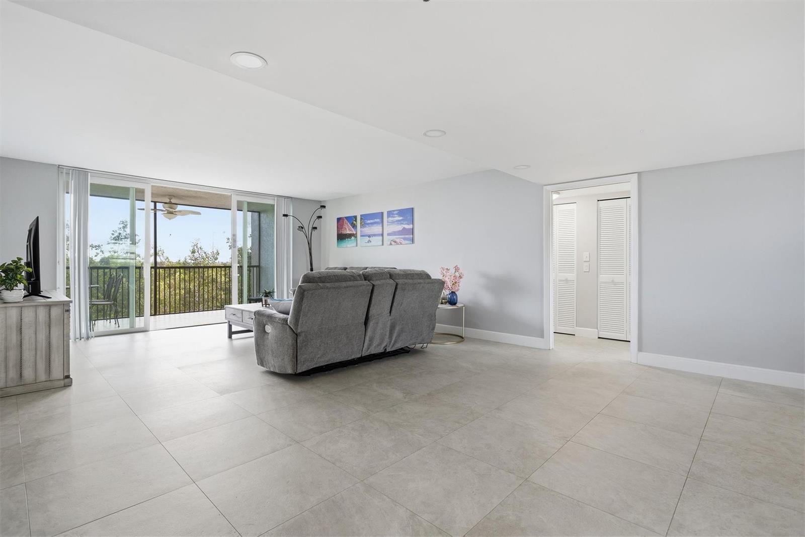 A living room features large light-colored floor tiles, a gray sofa, and a sliding glass door — 3910 Inverrary Boulevard # B, Lauderhill FL 33319, LAUDERHILL, FL