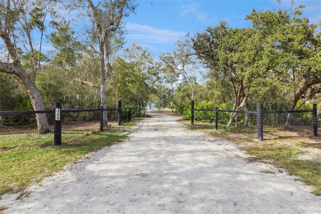 A dirt driveway leads through a gated entrance into a wooded property with wire fencing — 324 SUMMERVILLE LANE, SANFORD, FL