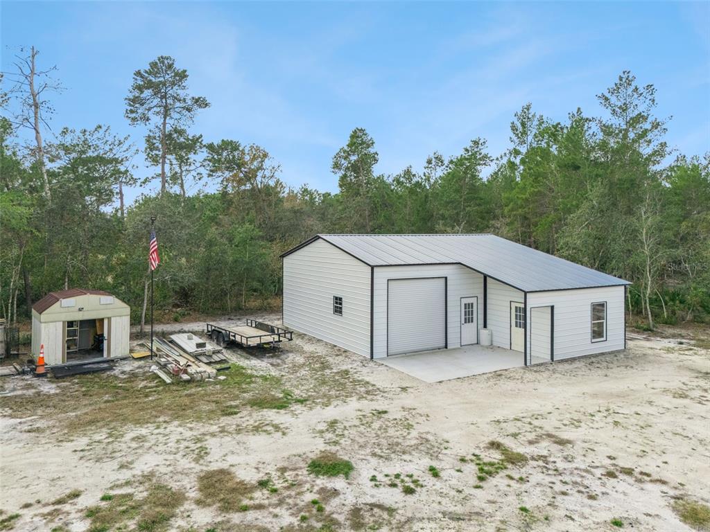 A metal workshop building stands on a sandy lot next to a small storage shed — 324 SUMMERVILLE LANE, SANFORD, FL