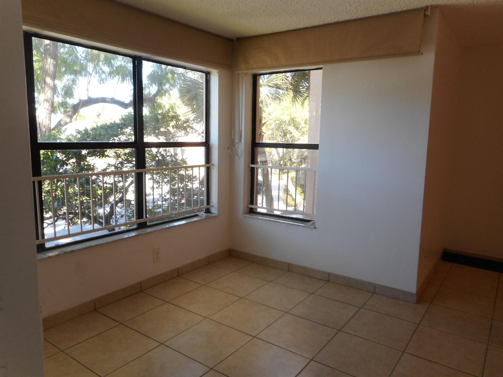 An empty room features beige tile flooring, white walls, and two windows with metal railings — 2900 S University Drive # 9210, Davie FL 33328, DAVIE, FL