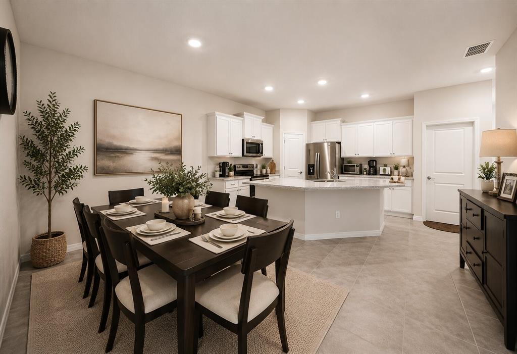A dining area with a dark wood table sits adjacent to an open-concept white kitchen — 31398 ANCIENT SAGE ROAD, WESLEY CHAPEL, FL