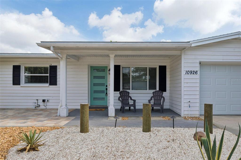 A white house exterior features a teal front door, a covered porch, and gravel landscaping — 10926 TEMPLE AVENUE, SEMINOLE, FL