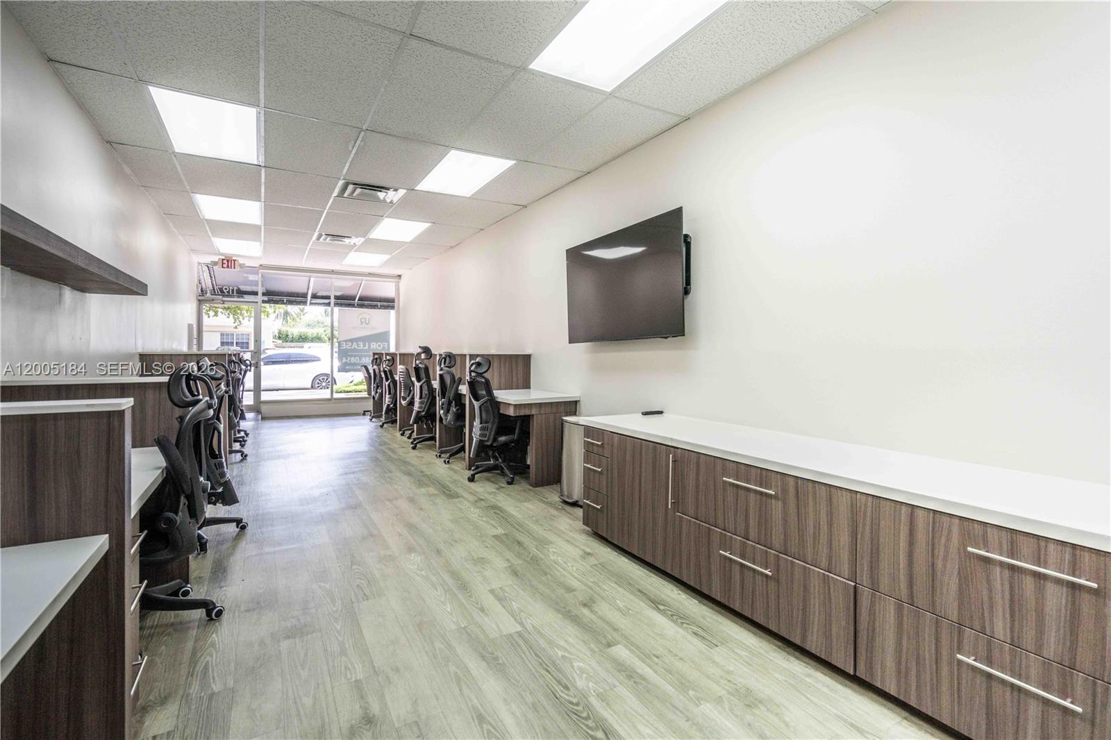 This office space features rows of desks with chairs, wood-grain cabinetry, and a wall-mounted television — 1197 71 St, Miami Beach FL 33141, MIAMI BEACH, FL
