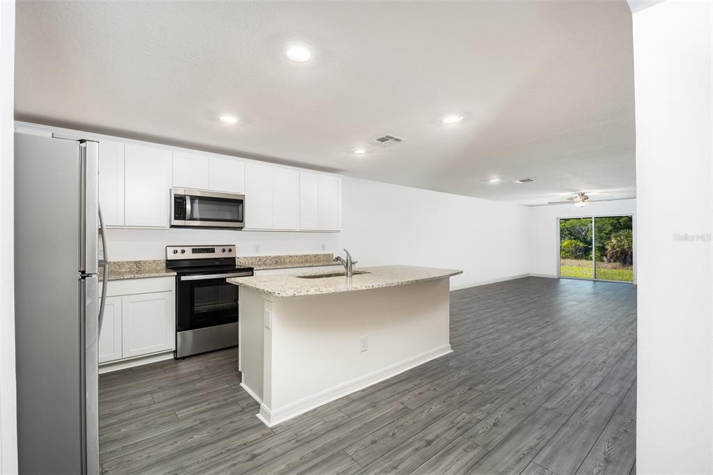 A kitchen with white cabinets, granite countertops, and stainless steel appliances opens to a living area — 3171 SEVILLE STREET, LAKE ALFRED, FL