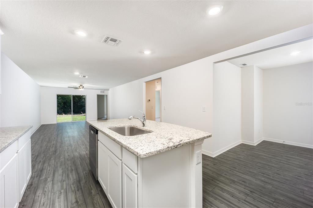 A kitchen island with a granite countertop and stainless steel sink overlooks a living area — 3171 SEVILLE STREET, LAKE ALFRED, FL