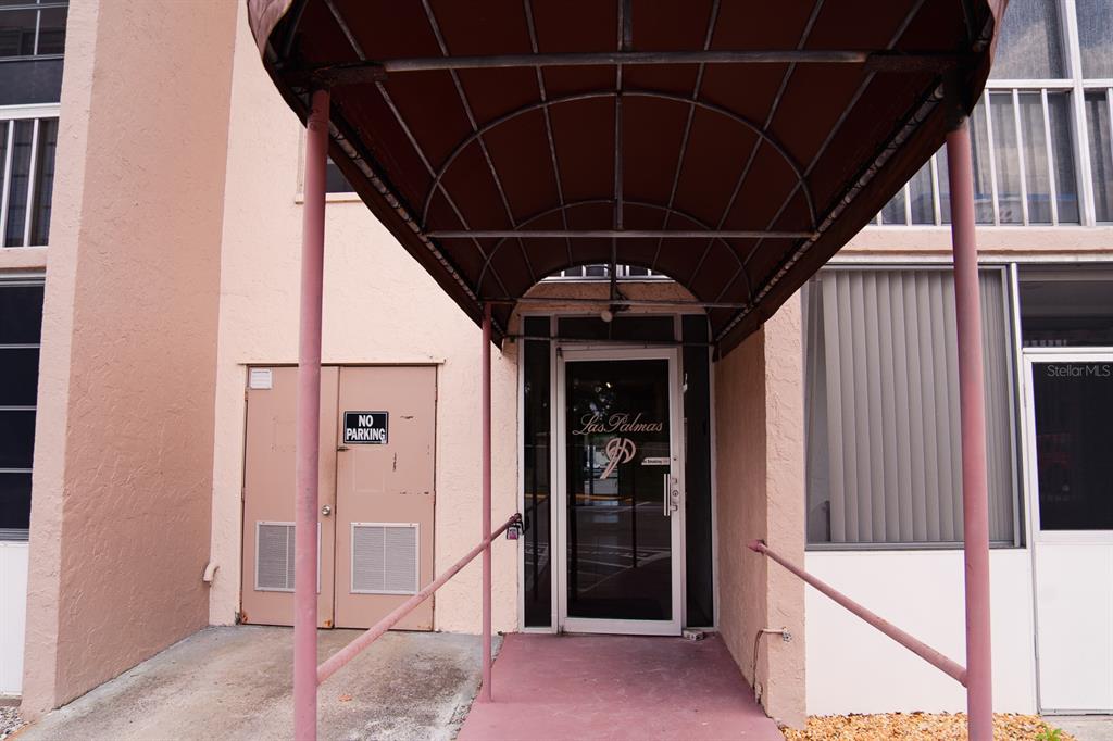 The exterior entrance to the Las Palmas building features a maroon awning over a glass door — 519 ALBEE FARM ROAD UNIT 110, VENICE, FL