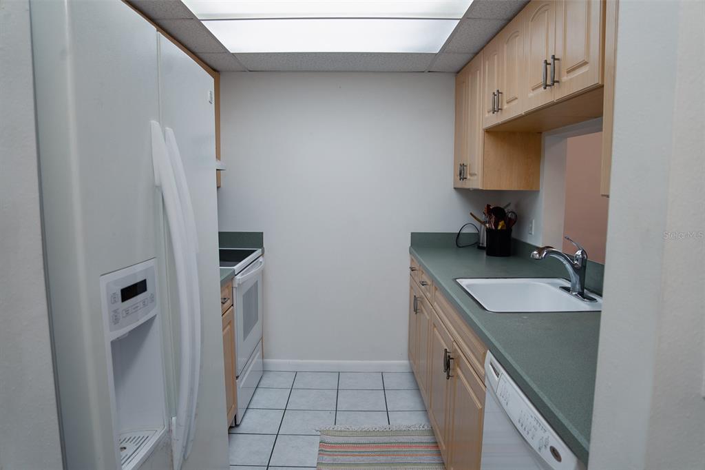 A galley kitchen features light wood cabinets, green countertops, white appliances, and tiled flooring — 519 ALBEE FARM ROAD UNIT 110, VENICE, FL