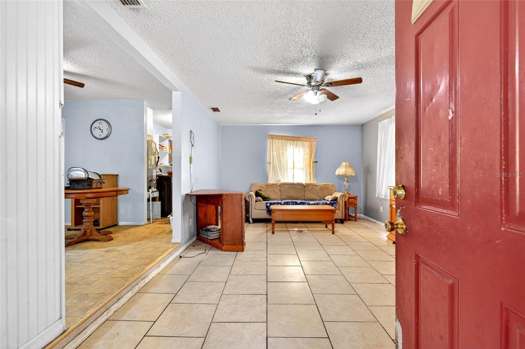 A view from a red doorway into a living room with tile floors and furniture — 3660 SE 139TH LANE, SUMMERFIELD, FL