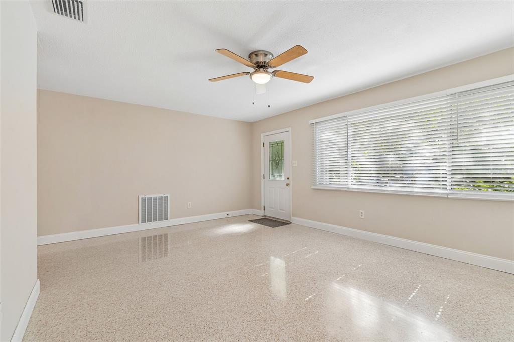 A bright room features light-colored walls, a ceiling fan, large windows, and terrazzo flooring — 200 EVELYN AVE, CLEARWATER, FL