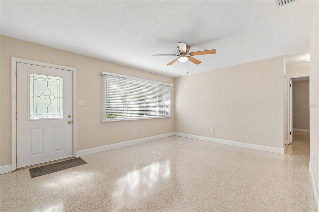 A bright, empty living room features light-colored walls, a ceiling fan, and speckled tile flooring — 200 EVELYN AVE, CLEARWATER, FL