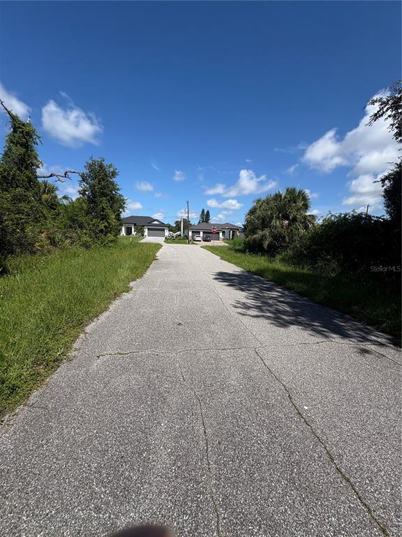 A paved road leads toward two houses under a blue sky with scattered clouds — 4128 KIRSTEN LANE, PORT CHARLOTTE, FL