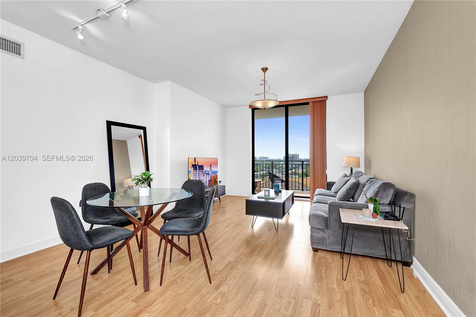 A living and dining area features wood-look flooring, a grey sofa, and a glass-topped table — 888 S Douglas Rd # 910, Coral Gables FL 33134, CORAL GABLES, FL