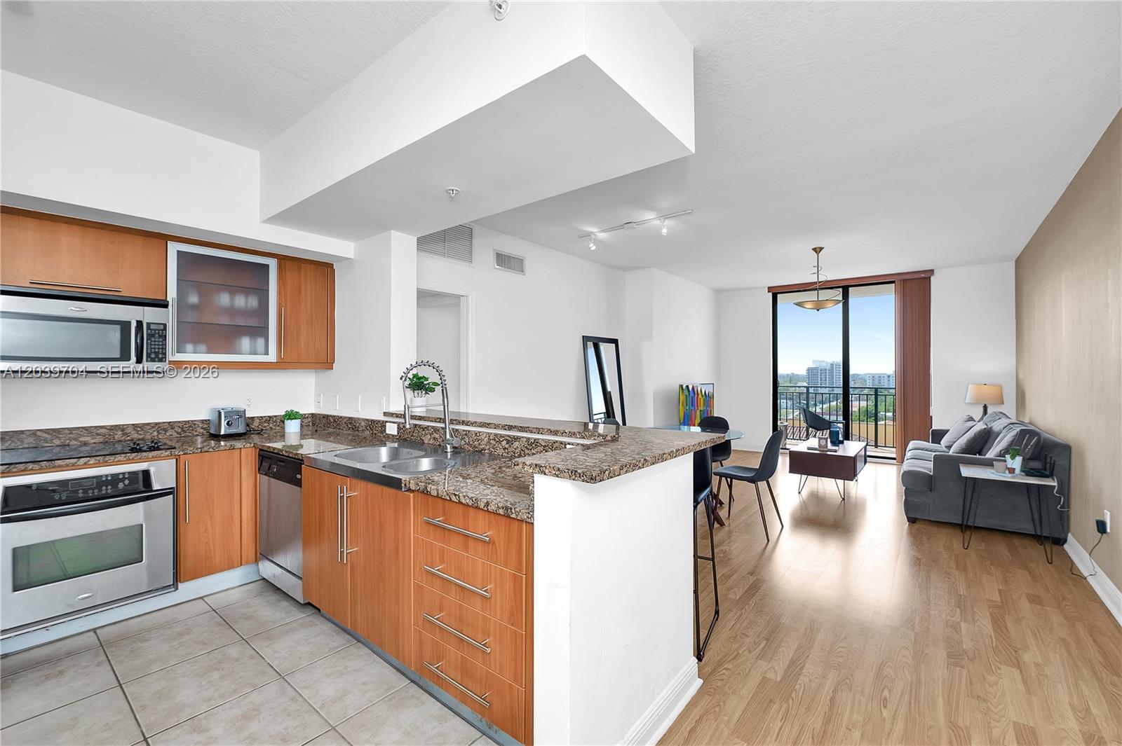 A kitchen with wood cabinets and granite countertops opens into a living area with balcony — 888 S Douglas Rd # 910, Coral Gables FL 33134, CORAL GABLES, FL