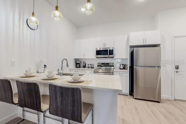 A modern kitchen features white cabinets, stainless steel appliances, and a breakfast bar with stools — 209 FAMAGUSTA DRIVE, DAVENPORT, FL