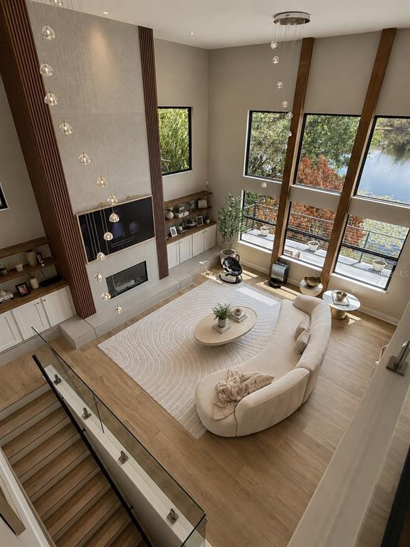 A high-ceilinged living room features a curved sofa, fireplace, and floor-to-ceiling windows overlooking water — 7826 PINE HAVEN COURT, ORLANDO, FL
