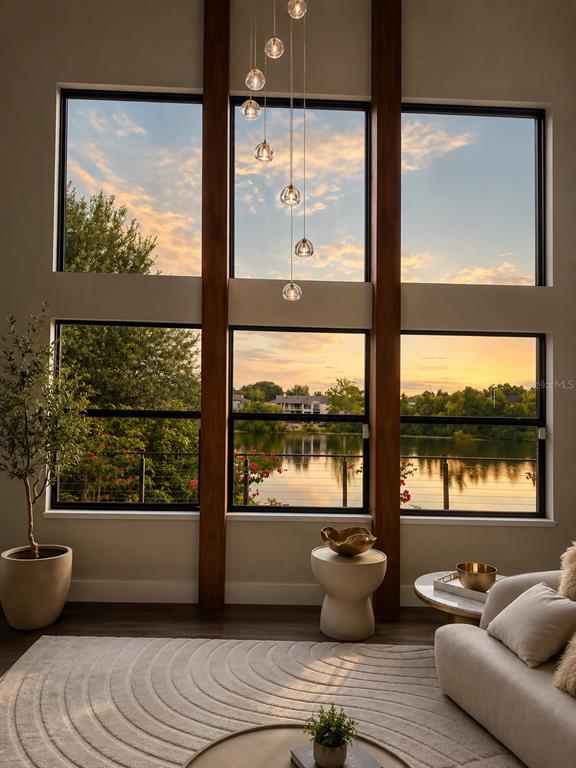 A living room features floor-to-ceiling windows overlooking a lake, a modern chandelier, and neutral furniture — 7826 PINE HAVEN COURT, ORLANDO, FL