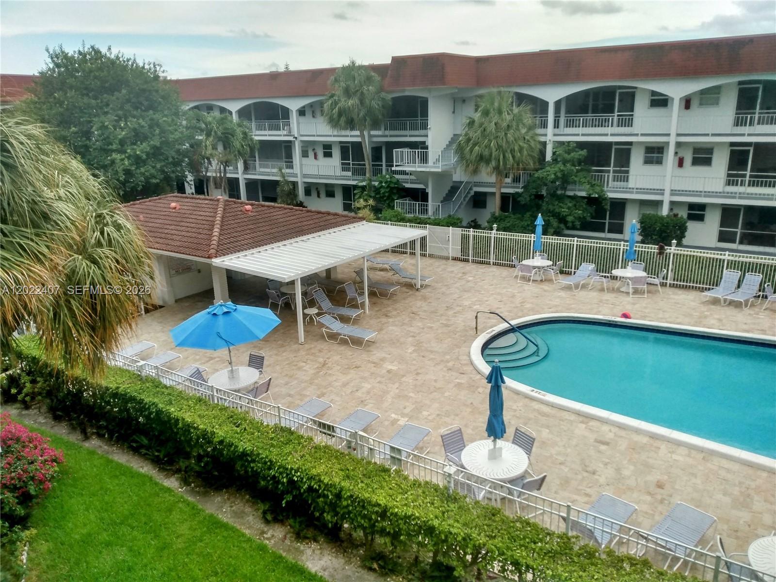 An outdoor swimming pool area with lounge chairs, tables, and a covered patio — 581 Blue Heron Dr # B, Hallandale Beach FL 33009, HALLANDALE BEACH, FL