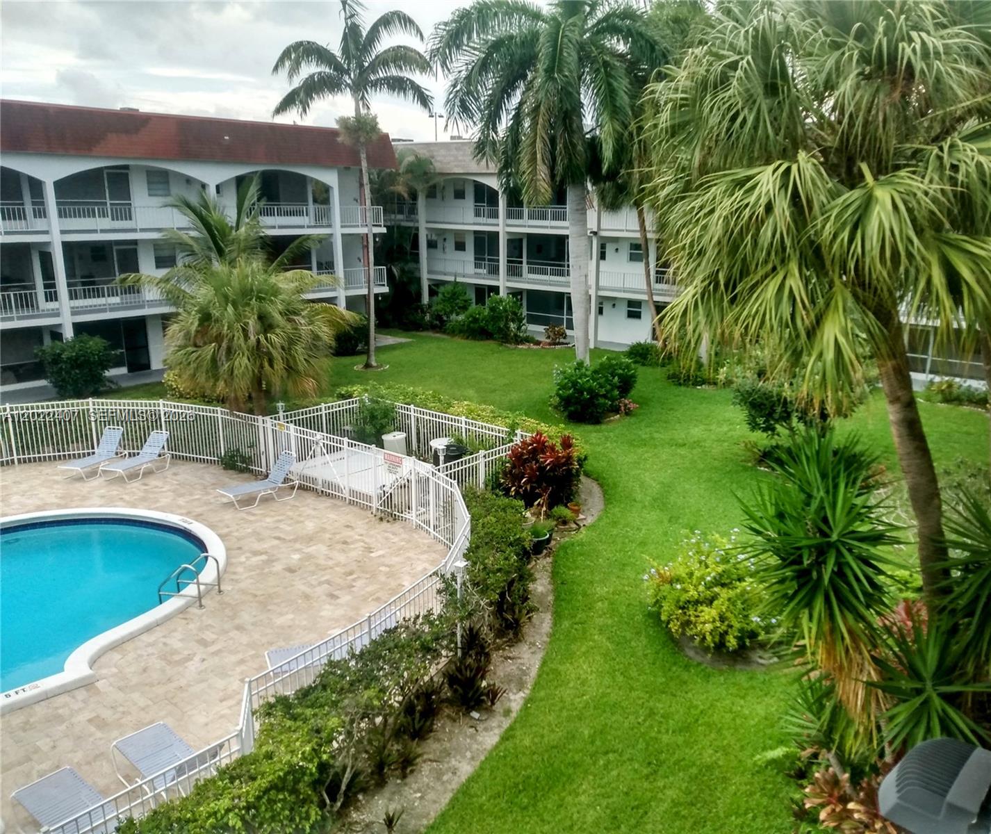 An elevated view of a swimming pool area surrounded by a lawn and apartment buildings — 581 Blue Heron Dr # B, Hallandale Beach FL 33009, HALLANDALE BEACH, FL