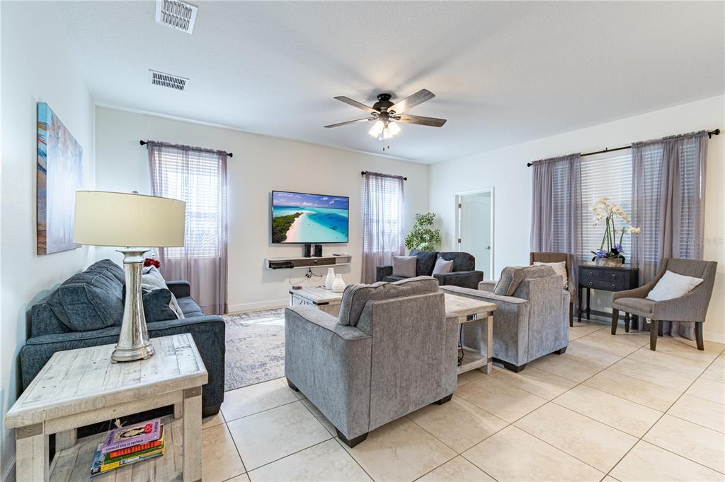 A living room features tile floors, a ceiling fan, a wall-mounted television, and neutral furniture — 9024 SHADOW MOUNTAIN STREET, DAVENPORT, FL