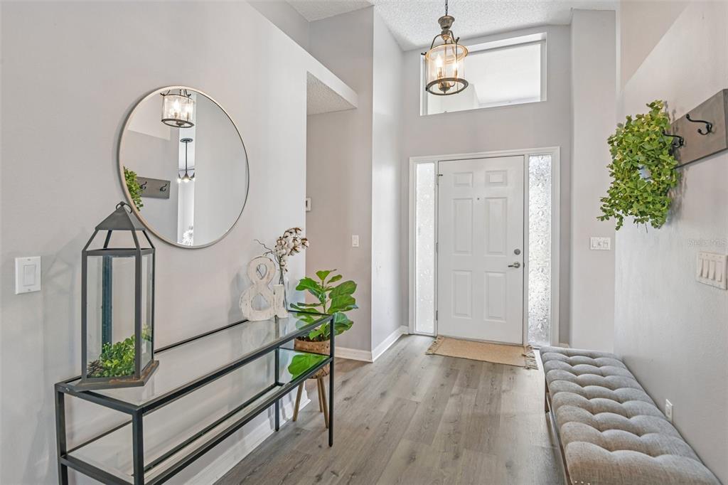 A bright entryway features a glass console table, a tufted bench, and a round mirror — 1129 DALESIDE LANE, NEW PORT RICHEY, FL