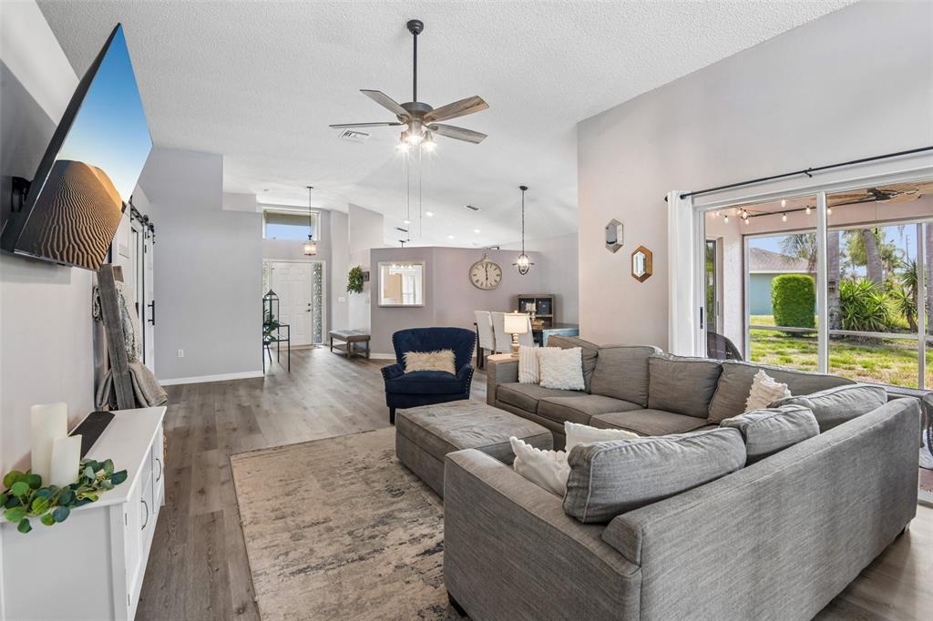 A living room features gray flooring, a sectional sofa, a ceiling fan, and sliding doors — 1129 DALESIDE LANE, NEW PORT RICHEY, FL