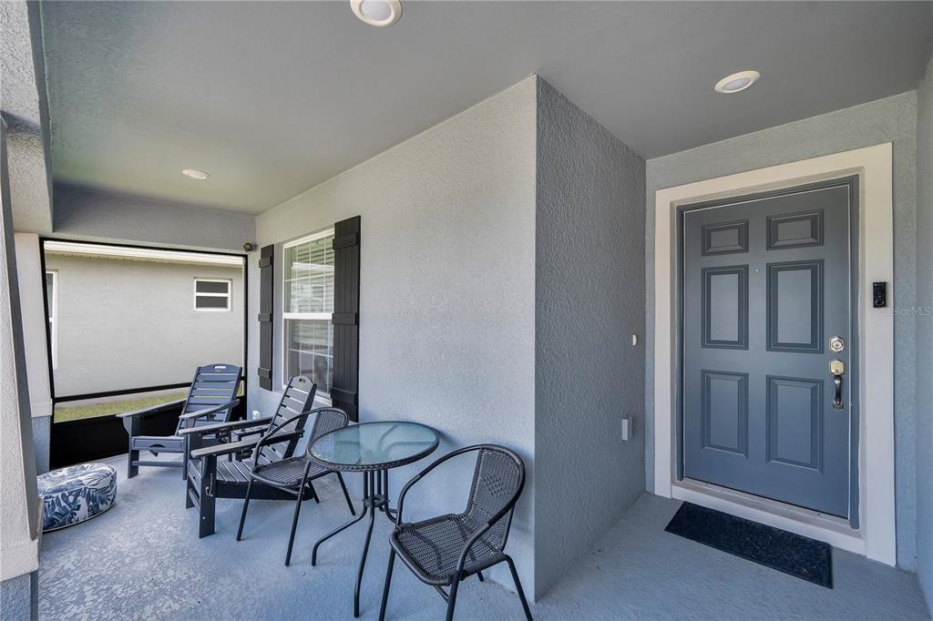 A covered front porch features gray walls, a blue door, and outdoor patio furniture — 2096 GOLDEN BEAK DRIVE, EAGLE LAKE, FL