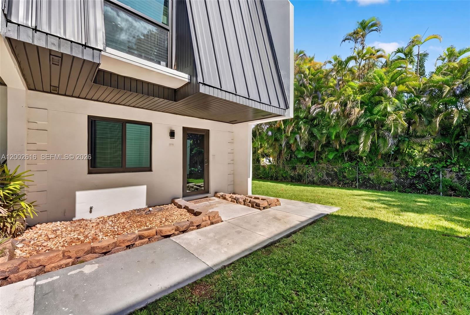 The exterior of a modern home features a metal-paneled overhang, a concrete walkway, and landscaping — 5555 Ludlam Rd # 23, South Miami FL 33155, SOUTH MIAMI, FL
