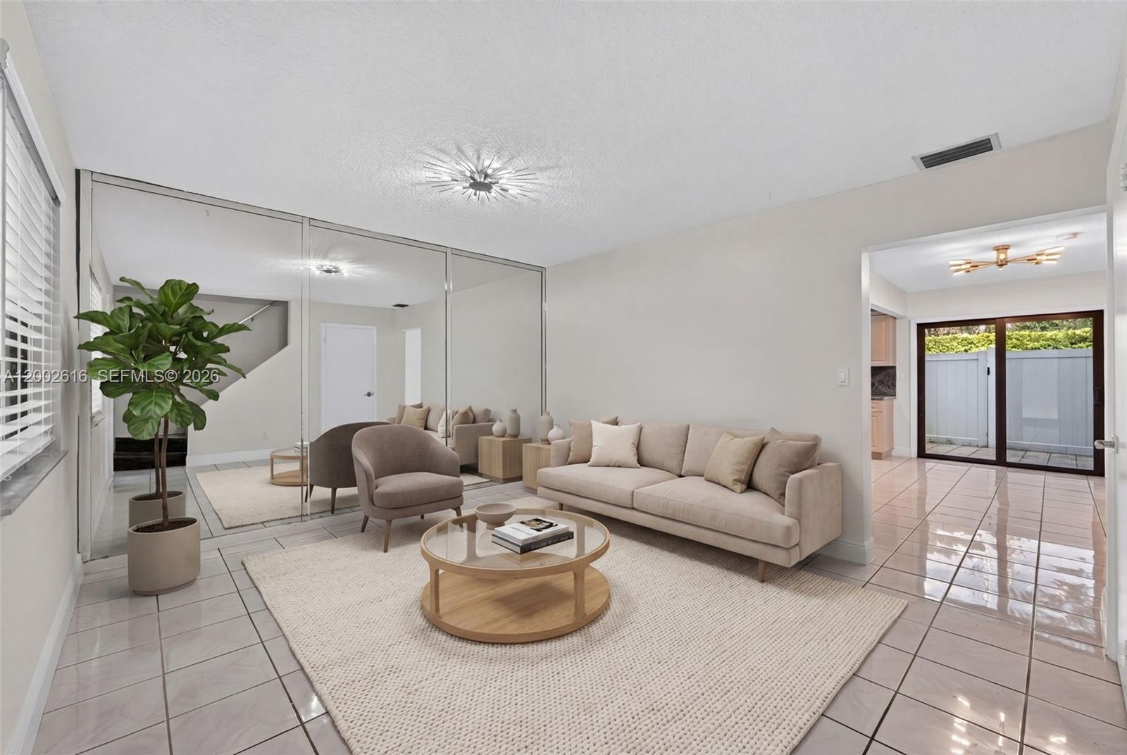 A living room features a beige sofa, a round coffee table, and a mirrored wall — 5555 Ludlam Rd # 23, South Miami FL 33155, SOUTH MIAMI, FL