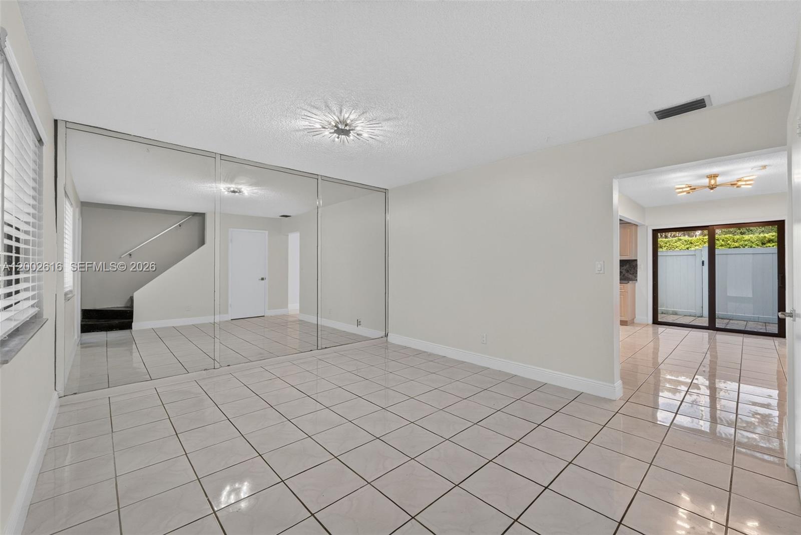 A room with light-colored tile floors, a mirrored wall, and an opening to a patio — 5555 Ludlam Rd # 23, South Miami FL 33155, SOUTH MIAMI, FL