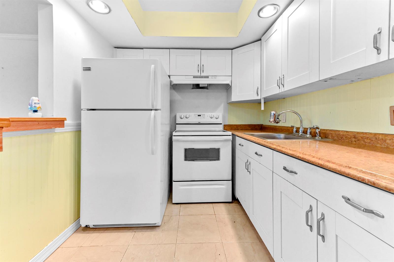 A kitchen features white cabinets, white appliances, and a tan countertop against yellow walls — 259 Newport P, Deerfield Beach FL 33442, DEERFIELD BEACH, FL