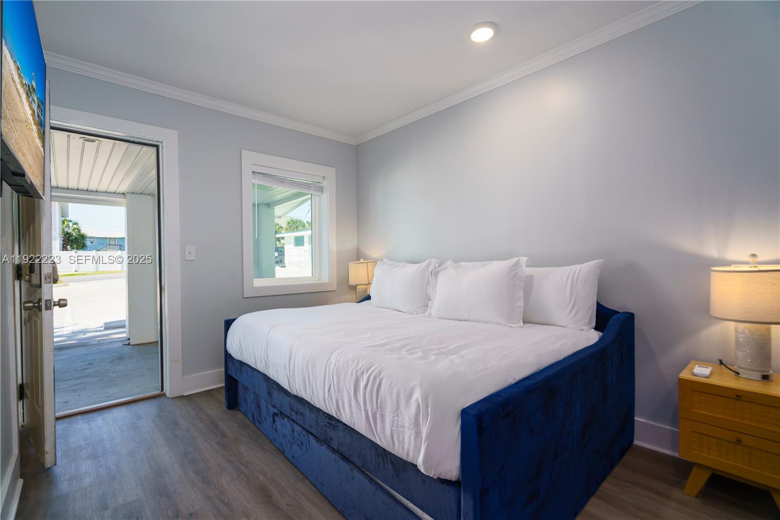A bedroom features a blue velvet daybed, a yellow nightstand, and a door leading outside — 17784 Front Beach Rd # 10, Panama City FL 32413, PANAMA CITY, FL