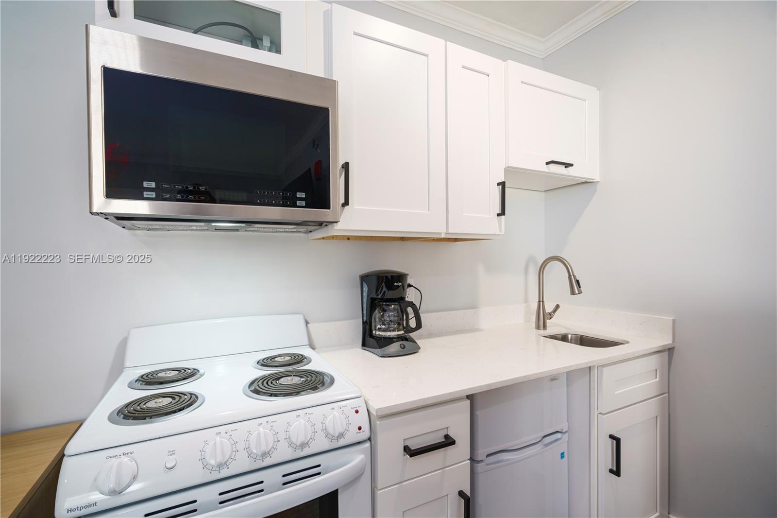A small kitchen features white cabinets, a white stove, a microwave, and a small sink — 17784 Front Beach Rd # 10, Panama City FL 32413, PANAMA CITY, FL